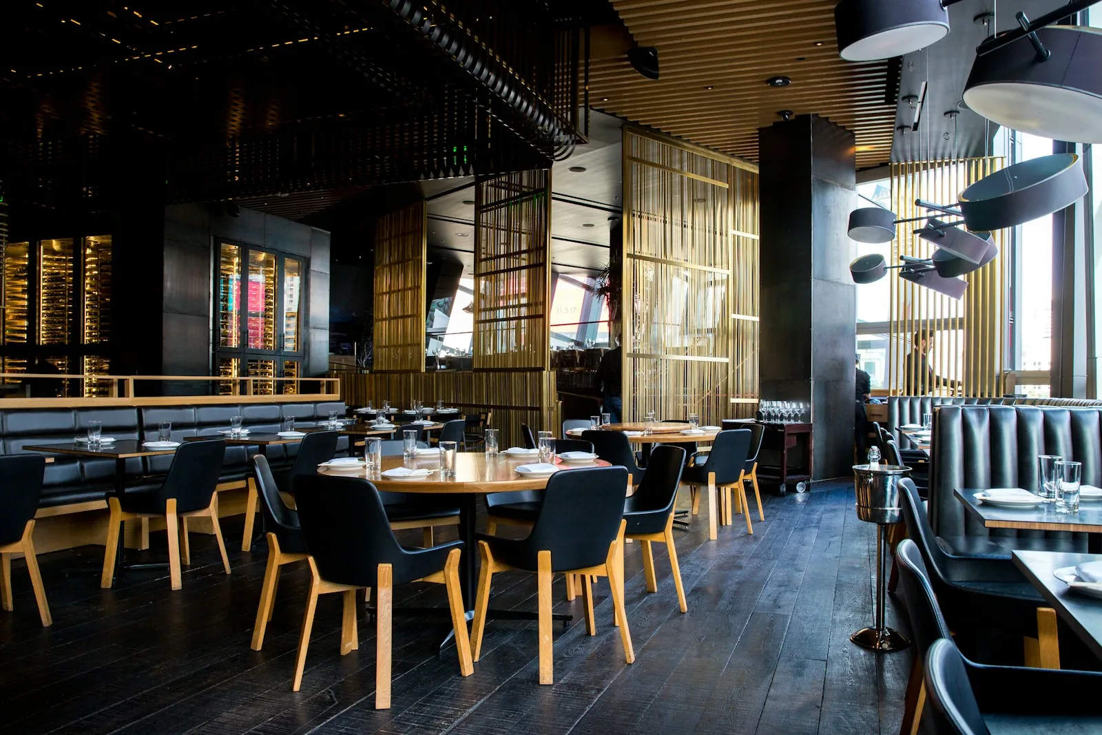 Sunlight across a restaurant interior with wooden tables, upholstered chairs and pendant lights